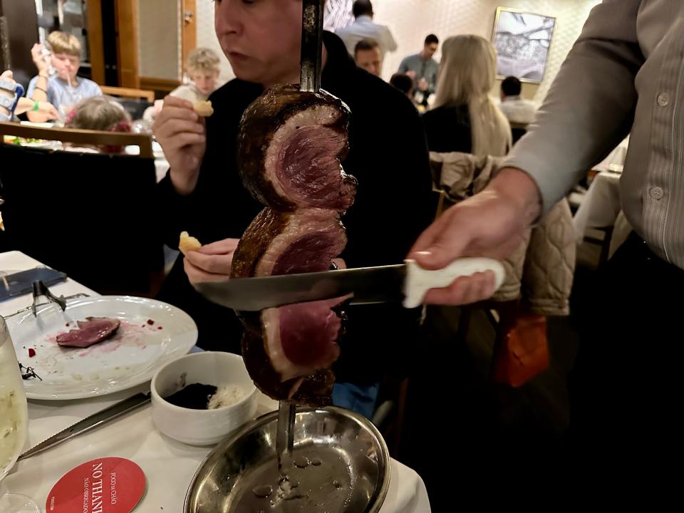 server carving skewered meat at a table in fogo de chao