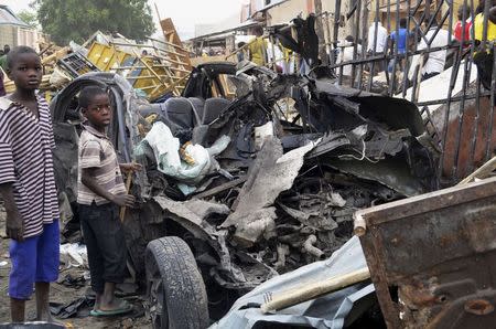 Two boys stand near the charred chassis of a vehicle after a bomb attack believed to have been carried out by the Islamist militant group Boko Haram that killed at least 10 people near a busy market area, in Ajilari-Gomari in Maiduguri in this March 2, 2014 file photo. REUTERS/Stringer/Files