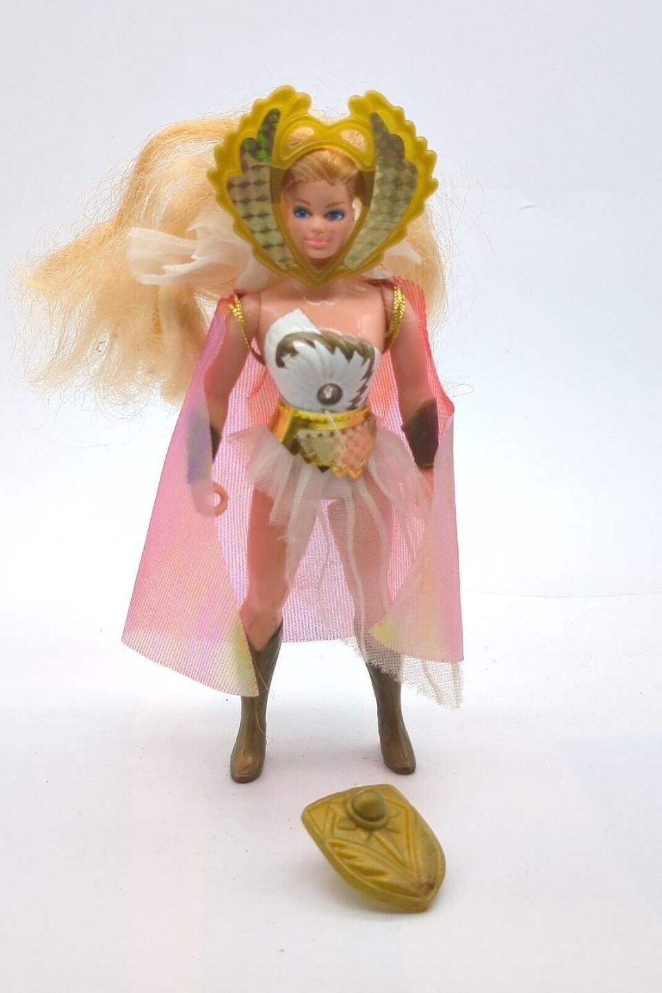 She-Ra action figure with blonde hair, gold headpiece, white and gold outfit, and pink cape