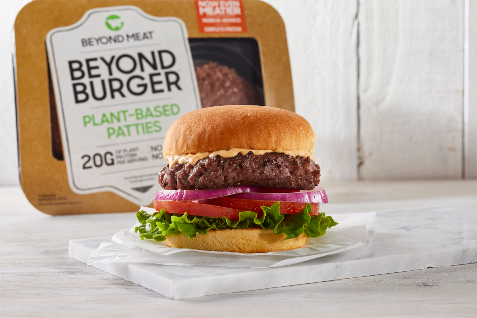 A Beyond Burger with cheese, with burgers in grocery-store packaging set behind it