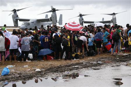 People wait to be airlifted to Manila as Ospreys from the U.S. Navy Ship (USNS) Charles Drew taxi on the tarmac in the background, at Tacloban airport November 14, 2013, in the aftermath of super typhoon Haiyan. REUTERS/Wolfgang Rattay