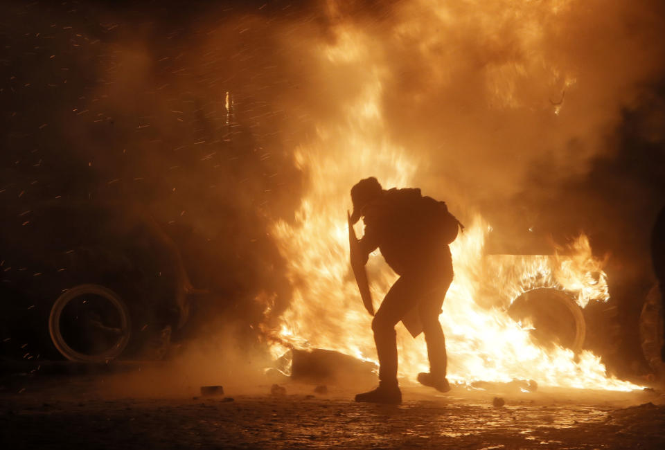 A protester throws a molotov cocktail towards a burning police car, in front of him, during clashes with police, in central Kiev, Ukraine, early Monday, Jan. 20, 2014. Anti-government protests in Ukraine's capital escalated into fiery street battles with police Sunday as thousands of demonstrators hurled rocks and firebombs to set police vehicles ablaze. Dozens of officers and protesters were injured. (AP Photo /Efrem Lukatsky)