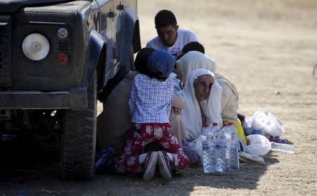 Migrants rest in the shade of a police jeep as they wait to continue their road north at a newly built registration and transit center near Gevgelija, Macedonia August 23, 2015. REUTERS/Ognen Teofilovski