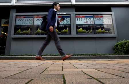 A passerby walks past an electronic boards Japan's Nikkei average, the Dow Jones Industrial Average and foreign exchange rates outside a brokerage in Tokyo, Japan, October 11, 2018. REUTERS/Issei Kato