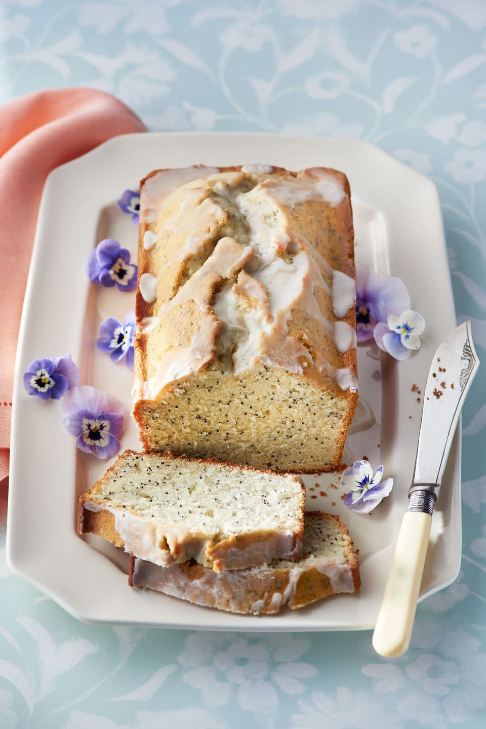 almond and poppy seed loaf cake on a white rectangle plate with pansies for garnish