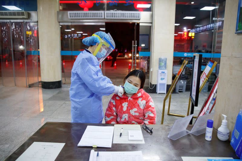 A nurse takes the temperature of a woman in the reception area of the First People's Hospital in Yueyang