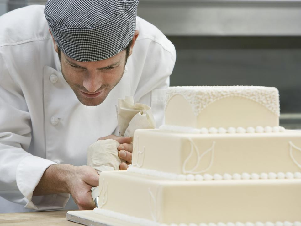 man decorating an all-white wedding cake