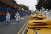 Workers in protective gears walk by dismantled barricaded lay along a shops after authorities' easing of COVID-19 curbs in Haizhu district in Guangzhou in south China's Guangdong province on Friday, Dec. 2, 2022. Local Chinese authorities on Saturday announced a further easing of COVID-19 curbs, with major cities such as Shenzhen and Beijing no longer requiring negative tests to take public transport. (Chinatopix Via AP)