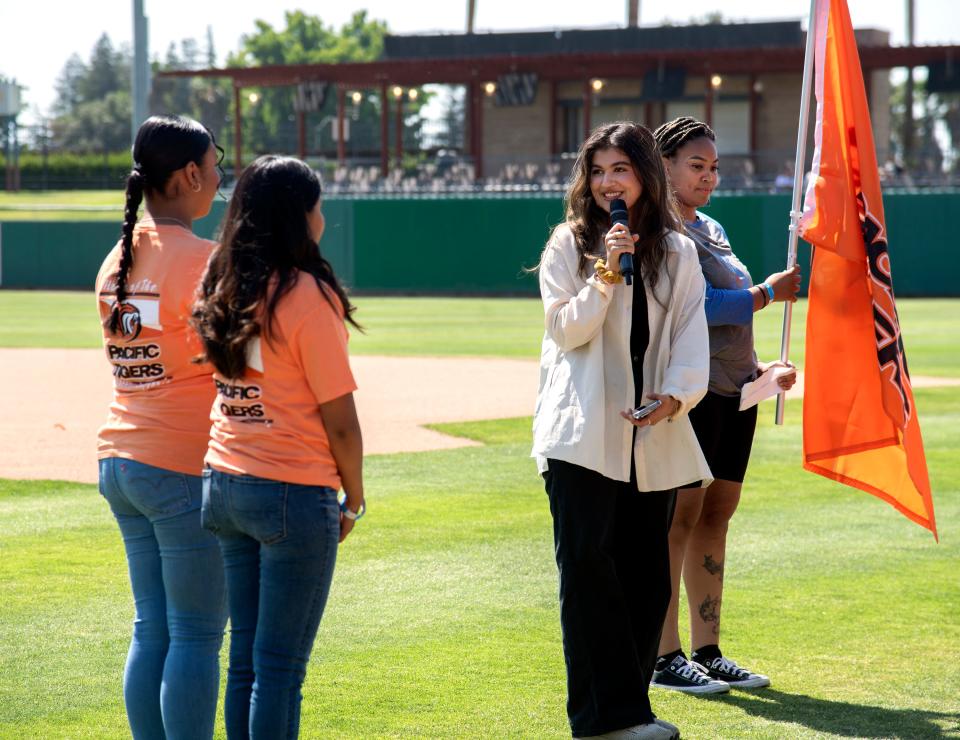 Stockton Scholars participants and University of the Pacific graduates Sahila Shah, center, and Mackenzi Gill, right, pass a Pacific flag to Pacific freshmen Gemma Hernandez, left, and Montserrat Cuanas, also program participants at the Stockton Scholars Rooted Rising event at the Stockton Ballpark in downtown Stockton on June 17, 2023.