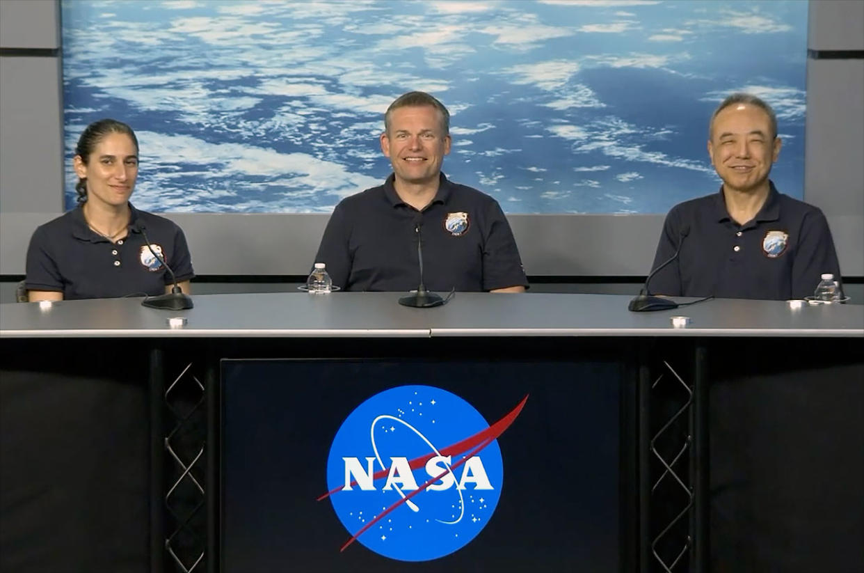  Two men and a woman in blue polo shirts sit at a table with a photo of earth as seen from space in the background. 