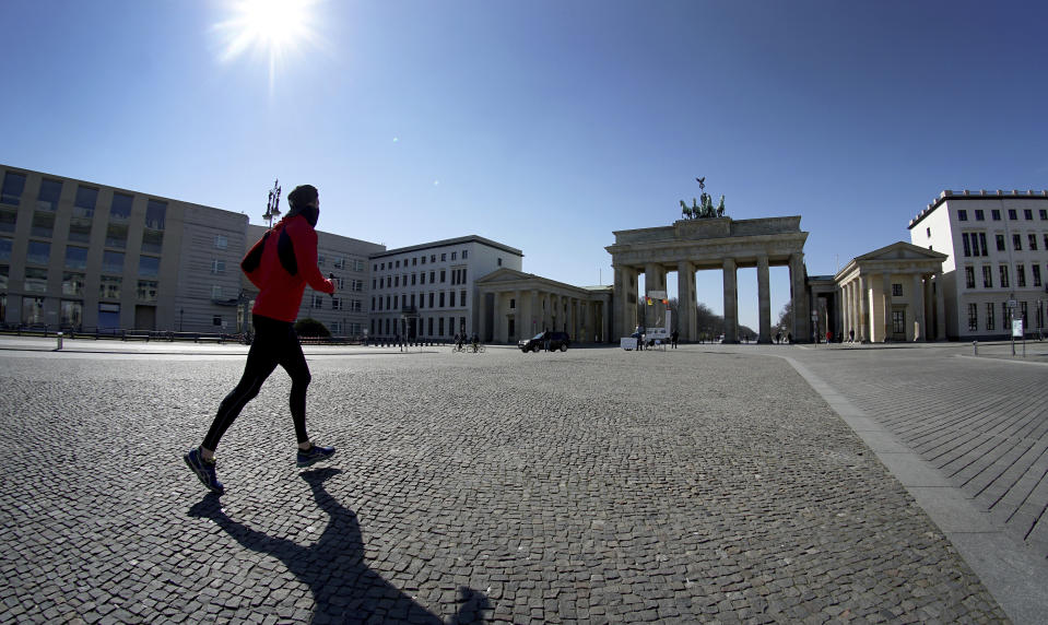FILE - In this March 24, 2020, file photo, a man jogs on the square in front of the Brandenburg Gate in Berlin, Germany. As the restrictions are eased, Chancellor Angela Merkel has pointed to South Korea as an example of how Germany will have to improve measures to “get ahead” of the pandemic with more testing and tracking of cases so that the rate of infections can be slowed. (AP Photo/Michael Sohn)