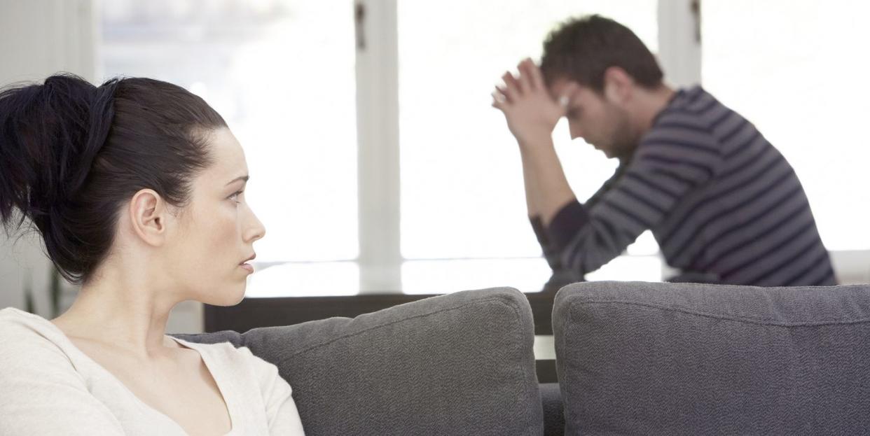 young woman sitting on sofa, looking at distressed man at table