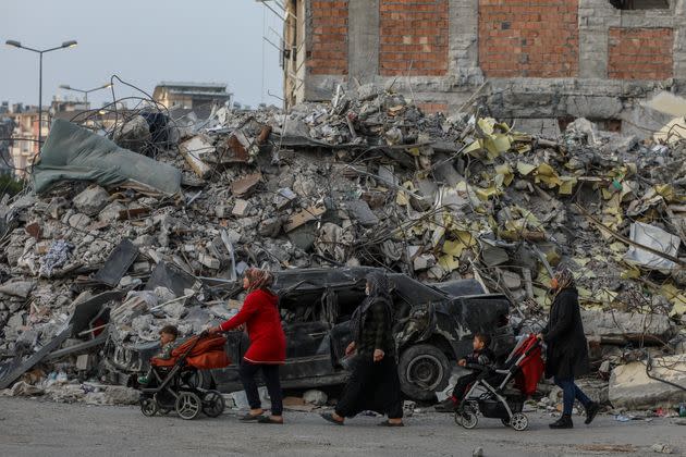 Women push children in strollers past a destroyed building on Feb. 28, 2023, in Iskenderun, Turkey.