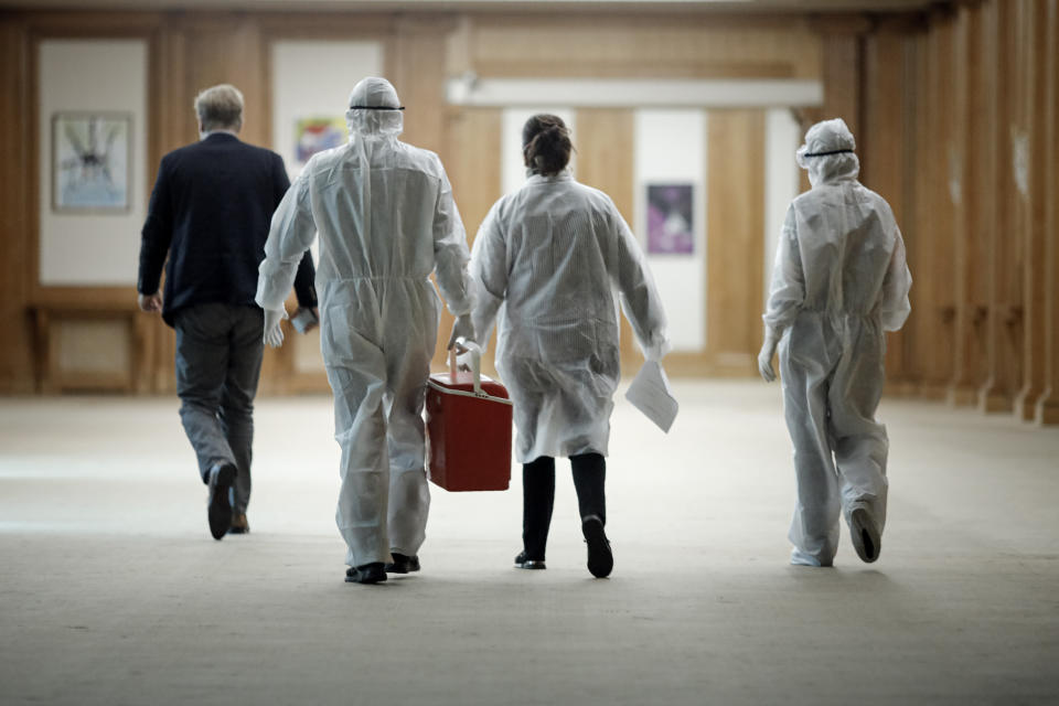 Health officials walk after taking samples for a coronavirus test from journalists and lawmakers in Bucharest, Romania, Friday, March 13, 2020 after it was confirmed that a senator who attended several meetings in the building tested positive for the infection. The caretaker prime minister of Romania, Ludovic Orban, said in a press conference at the parliament, the government, including all ministers, as well as the leadership of the ruling National Liberal Party and all its senators, are going into quarantine after one of the governing party's senators, who took part in high-level meetings, who confirmed to be infected with the coronavirus. (AP Photo/George Calin)