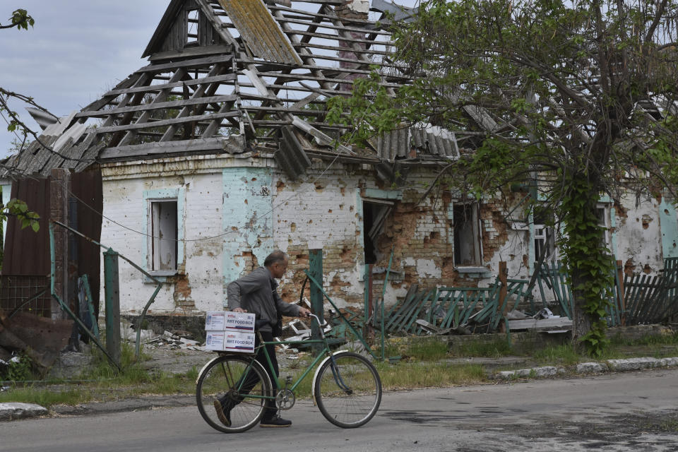 A local man hauls a bicycle with humanitarian aid in front of a house which was destroyed by Russian shelling in Orihiv, Ukraine, on Monday, May 22, 2023. (AP Photo/Andriy Andriyenko)
