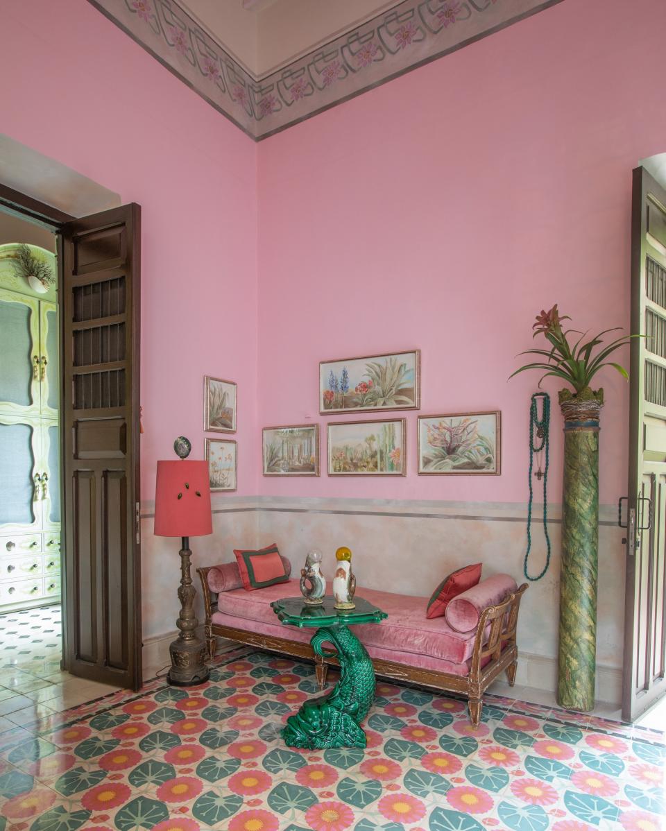 A sitting area in the primary bedroom contains a 19th-century French settee, an antique English majolica side table, and a vintage Chinese floor lamp. Skouras commissioned a series of watercolors from Allison Cosmos based on the flora of her native California. The primary bedroom required new flooring, so Skouras chose new tiles that were in keeping with the rest of the Art Nouveau flooring in the home.
