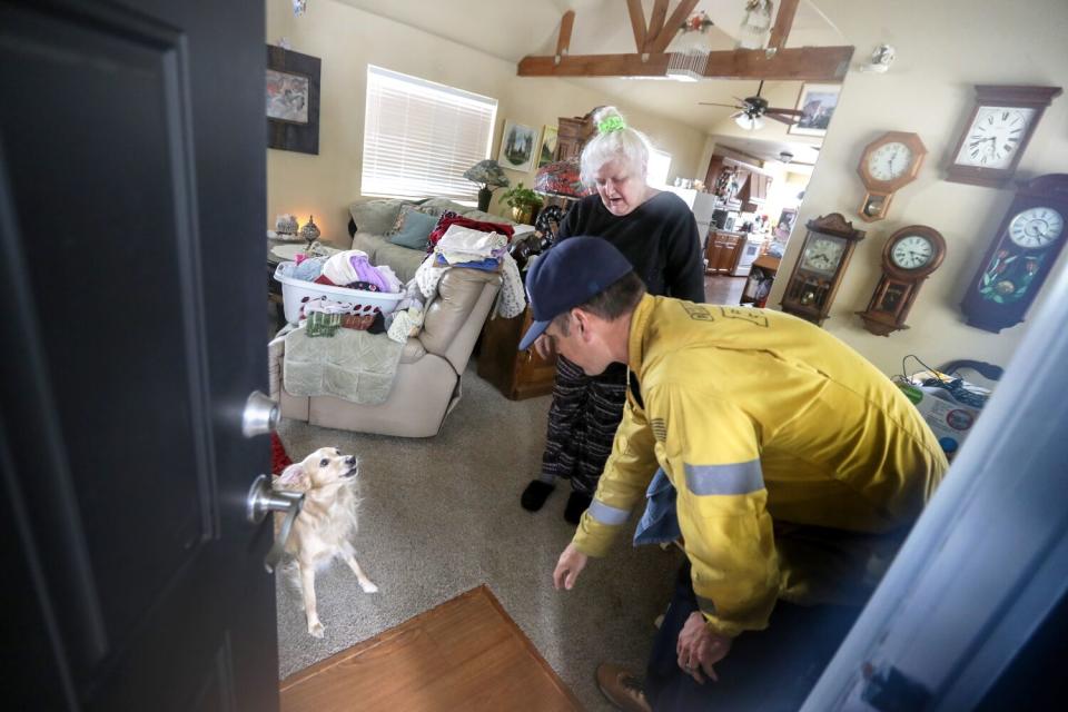 View from outside the front door - a firefighter stands just inside leaning down toward a small dog while a woman looks on.