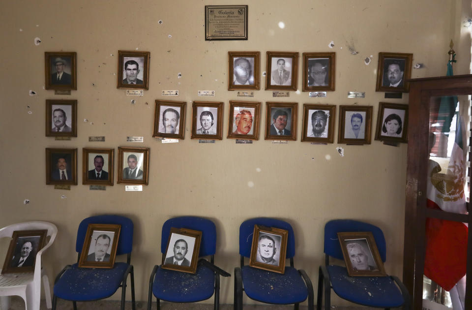 Portraits of former mayors hang on a City Hall wall riddled with bullet holes after a gun battle, in Villa Union, Mexico, Monday, Dec. 2, 2019. Dozens of pickup trucks crowded with armed men and mounted machine guns roared into Villa Union on Saturday. What followed were hours-long gun battles between a cartel force and state police that left 23 people dead. (AP Photo/Eduardo Verdugo)