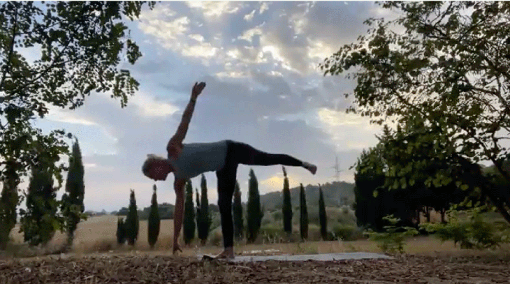 Woman practicing yoga outside at sunrise on her mat in a balancing pose
