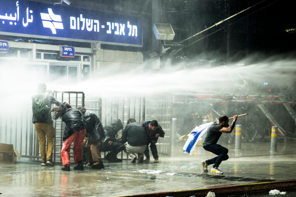 Israeli protesters run as police officers use water canon after clashes erupted during a demonstration against the government's judicial overhaul on March 27, 2023 in Tel Aviv, Israel.