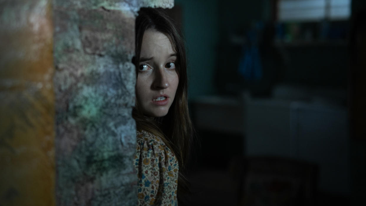  Kaitlyn Dever peeking around a corner with a look of fright in No One Will Save You. 