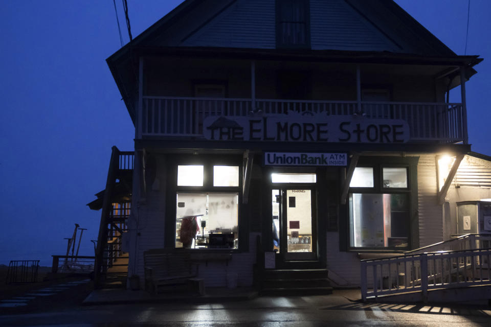 Robin Pough raises a window blind as she arrives to open the Elmore Store at dawn, Monday, March 4, 2024, in Elmore, Vt. The heartbeat of the town is the store. "I've always said it's a live, living, breathing creature. I don't own it; she owns me," says Kathy Miller, 63, who bought the store with her husband, Warren, in 1983. People would come in not only to buy milk and pick up the mail but to use the fax machine, find a plumber or just to swap gossip. (AP Photo/David Goldman)