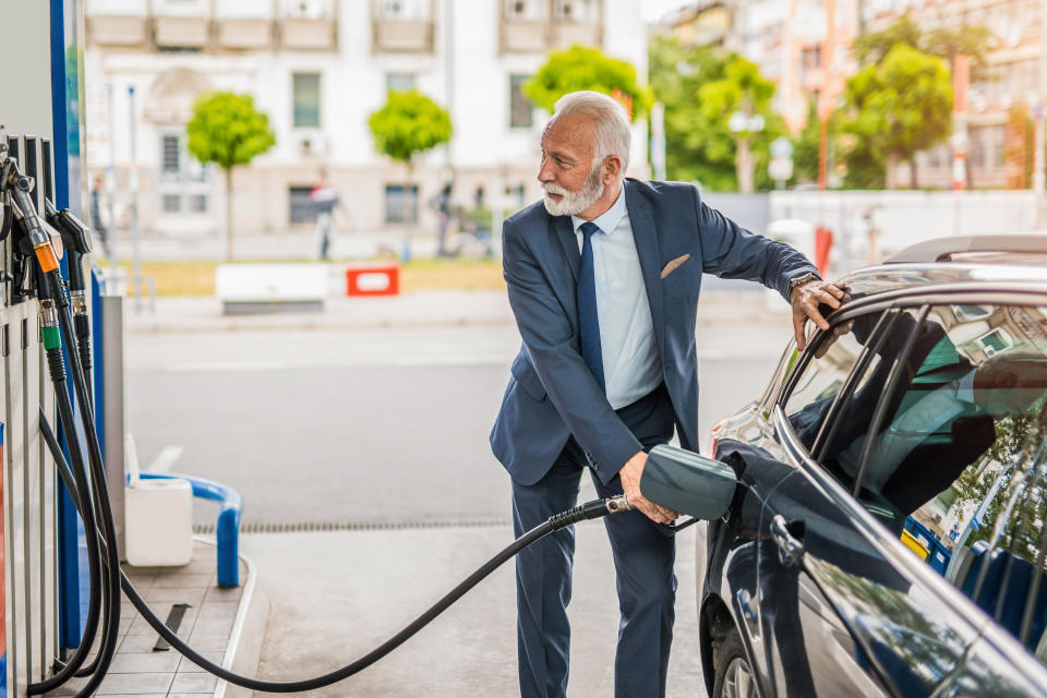 Senior businessman sipping fuel into car tank at gas station.