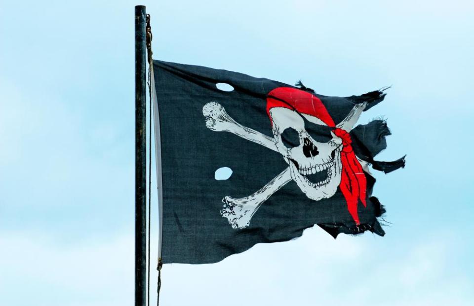 Torn skull and crossbones pirate flag against blue sky