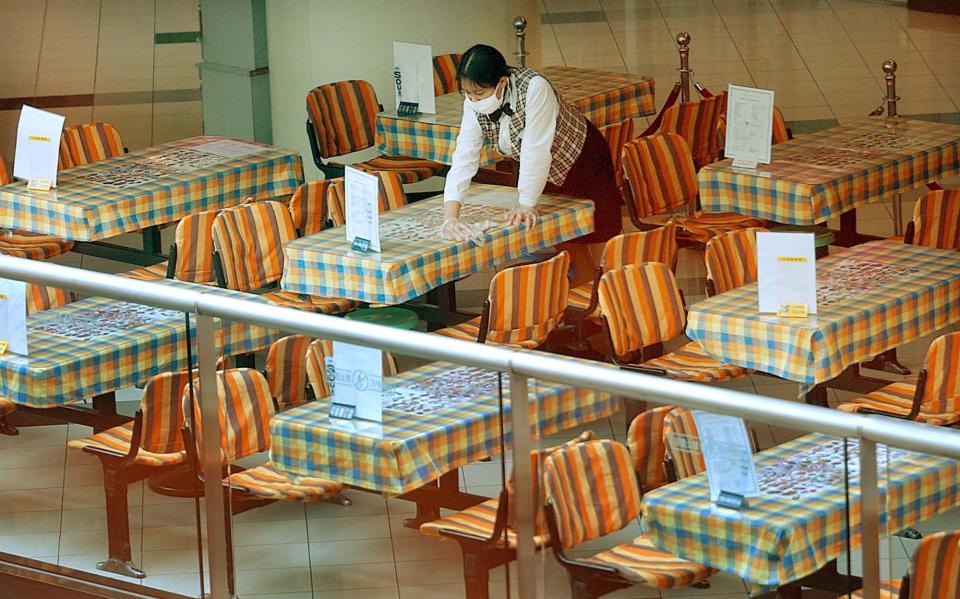 A masked employee cleans a table at an empty restaurant Monday, May 26, 2003 in Beijing.