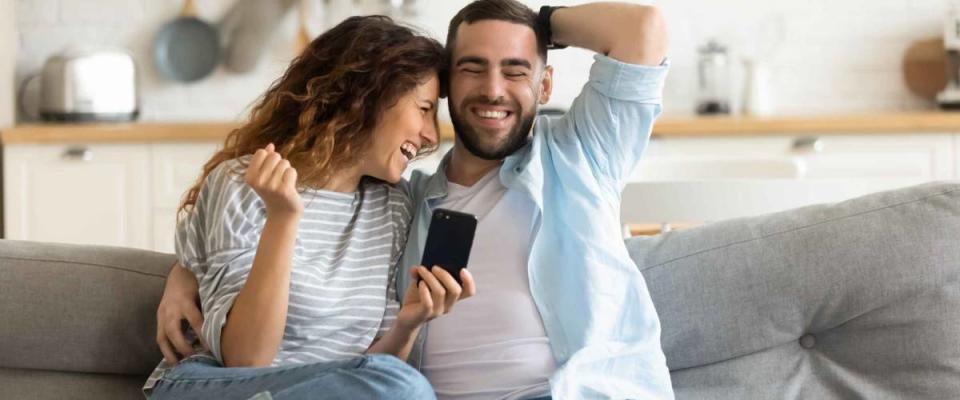 Cheerful married couple resting on couch looking at phone