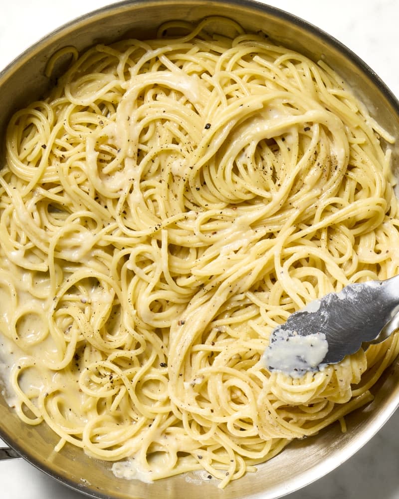 overhead shot of cacio e pepe in a pot with tongs.