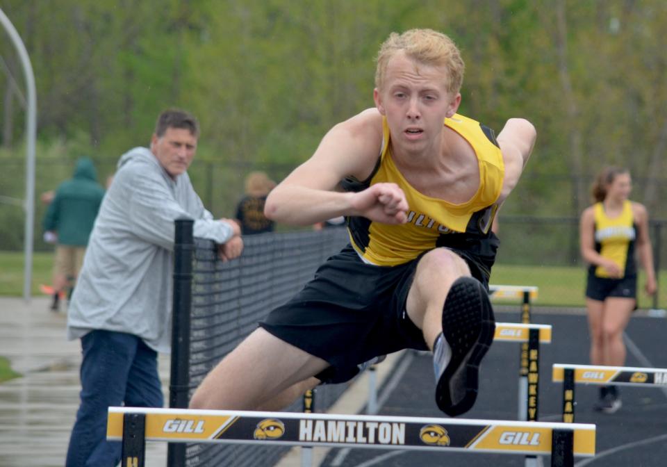 Hamilton's Owen Alderink hurdles as coach Kevin Spotts looks on.