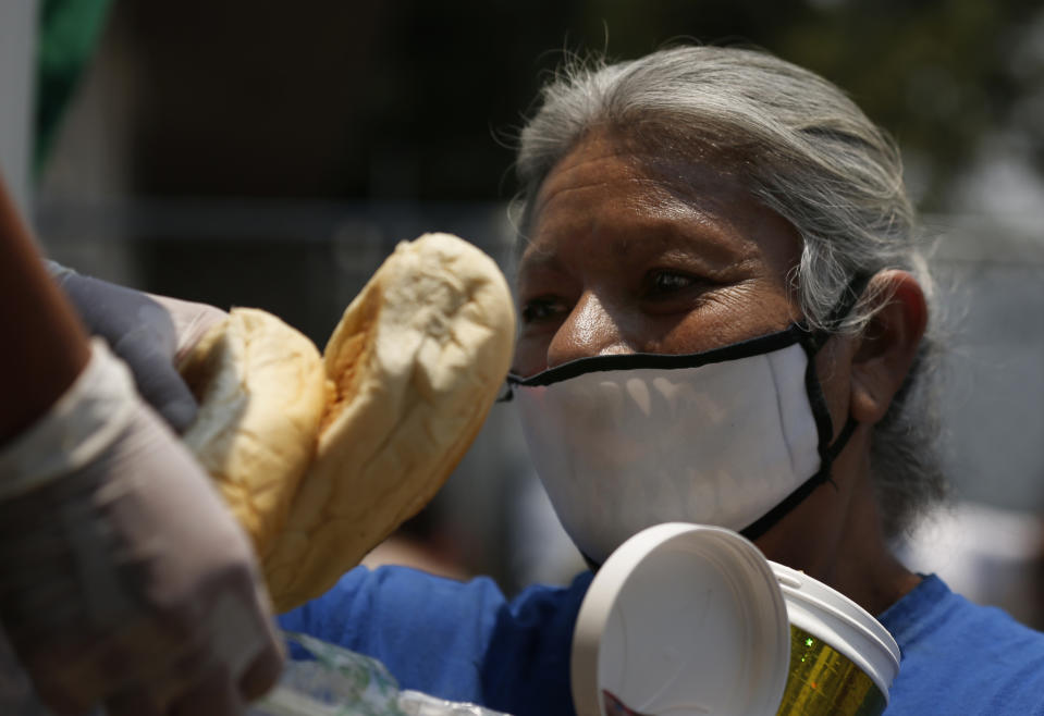 A woman gets a meal from the mobile dining rooms program as people who have not been able to work because of the COVID-19 pandemic line up for a meal outside the Iztapalapa hospital in Mexico City, Wednesday, May 20, 2020. (AP Photo/Marco Ugarte)