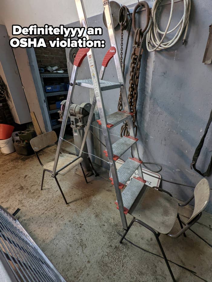 A metal stepladder placed sideways on four chairs in a workshop with tools and equipment hanging on the walls