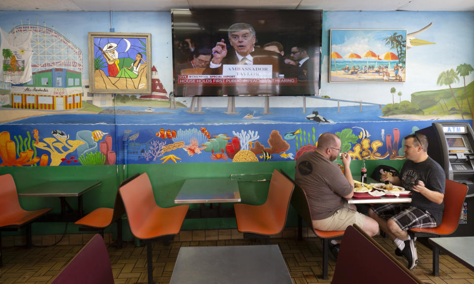 Two men eat Mexican food at Mr. Ruriberto's Taco Shop as U.S. diplomat in Ukraine, William Taylor, is seen on a television screen testifying before the House Intelligence Committee during the first public impeachment hearing of President Donald Trump's efforts to tie U.S. aid for Ukraine to investigations of his political opponents, Wednesday, Nov. 13, 2019, in San Diego. (AP Photo/Gregory Bull)