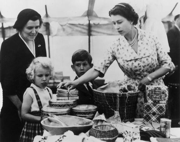 22nd August 1955:  Queen  Elizabeth II with Princess Anne, Prince Charles and their nurse, Helen Lightbody, at a stall during a Sale of Work event in Abergeldie Castle, near Balmoral Castle in Aberdeenshire. They are raising funds for the building of a new vestry at Craithie Church.  (Photo by Fox Photos/Getty Images)