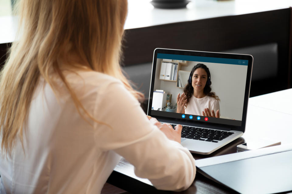 Rear back view young woman holding video call conversation with female colleague in wireless headphones, discussing working issues remotely or taking educational online class, self-isolation concept.