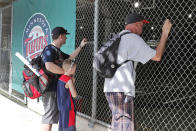 FILE - In this March 12, 2020, file photo, baseball fans look through a fence at Hammond Stadium after a game between the Minnesota Twins and the Baltimore Orioles was canceled, in Fort Myers, Fla. On MLB’s opening day, ballparks will be empty with the start of the season on hold because of the coronavirus pandemic. (AP Photo/Elise Amendola, File)