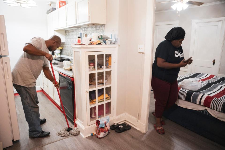 Scott mops the floor in the kitchen of their apartment at the Almadura while Harris catches up on emails about potential job opportunities. They used red tape to seal cracks along their appliances and baseboards where they found pests entering.