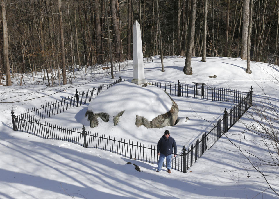 Randy Patten poses in front of the Ephraim Williams Jr. memorial on Wednesday, Feb. 26, 2014, in Lake George, N.Y. In the 1990s, businessman Anthony Tomasovic was granted permission to fill in his vacant, sloping property bordering the ravine where British Colonial troops and their Mohawk Indian allies were ambushed by a larger force of French and Indians in 1755. The land borders the wooded ravine where about 1,000 British Colonial troops and 200 of their Mohawk Indian allies were ambushed by a larger force of French and Indians on the morning of Sept. 8, 1755. Patten is convinced many of the scores of casualties from the ambush were buried afterward in the ravine. (AP Photo/Mike Groll)