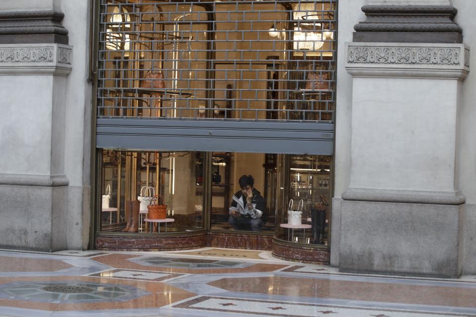 FILE - In this Wednesday, March 11, 2020 filer, a cleaner sits in a shut down shop at the Vittorio Emanuele shopping arcade in Milan, Italy. The eurozone's third-largest economy and a major exporter, Italy on Wednesday becomes the first western industrialized nation to idle swaths of industrial production to stop the spread of coronavirus by keeping yet more of the population at home. The new coronavirus causes mild or moderate symptoms for most people, but for some, especially older adults and people with existing health problems, it can cause more severe illness or death. (AP Photo/Luca Bruno, File)