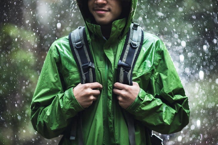 A young adult man goes for a hike in the rain with the raindrops repelling from his raincoat.