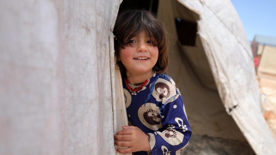 A child poses for a photo from a makeshift shelter at Al-Tehh camp for Syrians in Idlib (EPA)