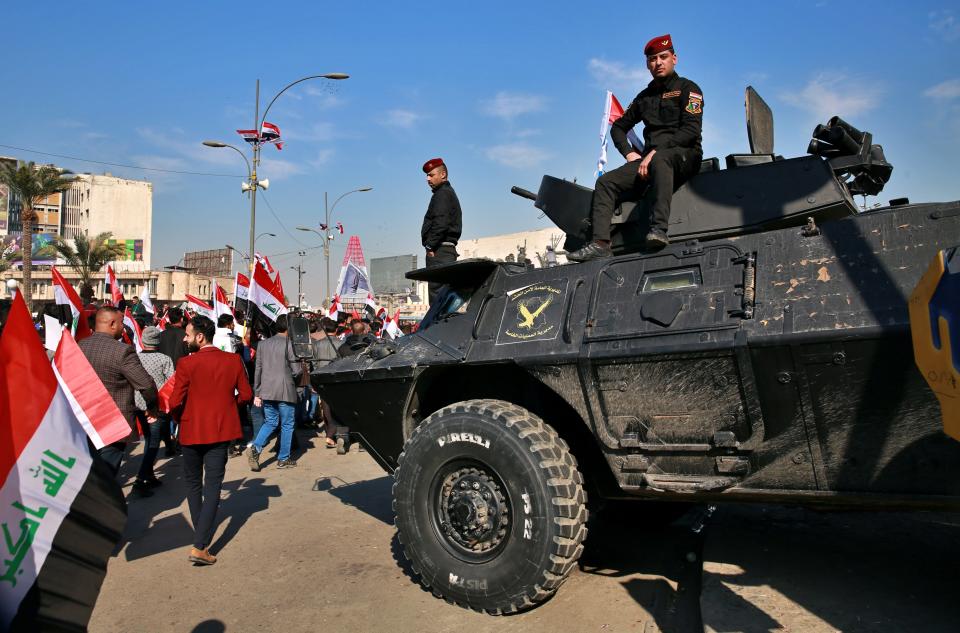 Security forces stand guard while supporters of Popular Mobilization Forces protest, in Tahrir Square, Iraq, Sunday, Jan. 3, 2021. Thousands of Iraqis converged on a landmark central square in Baghdad on Sunday to commemorate the anniversary of the killing of Abu Mahdi al-Muhandis, deputy commander of the Popular Mobilization Forces, and General Qassem Soleimani, head of Iran's Quds force in a U.S. drone strike. (AP Photo/Khalid Mohammed)