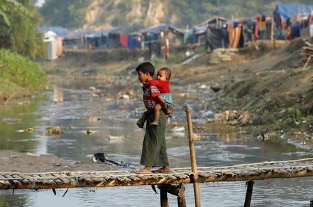 A Rohingya refugee child, carrying another child, walks along a bridge from no-man's land to Bangladesh, at the Bangladesh-Myanmar border near Cox's Bazar, Bangladesh January 12, 2018. REUTERS/Tyrone Siu