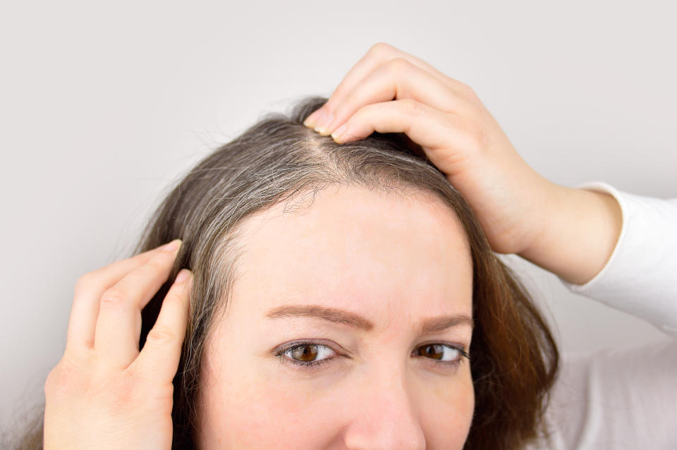 Woman is checking hair for greys in a mirror