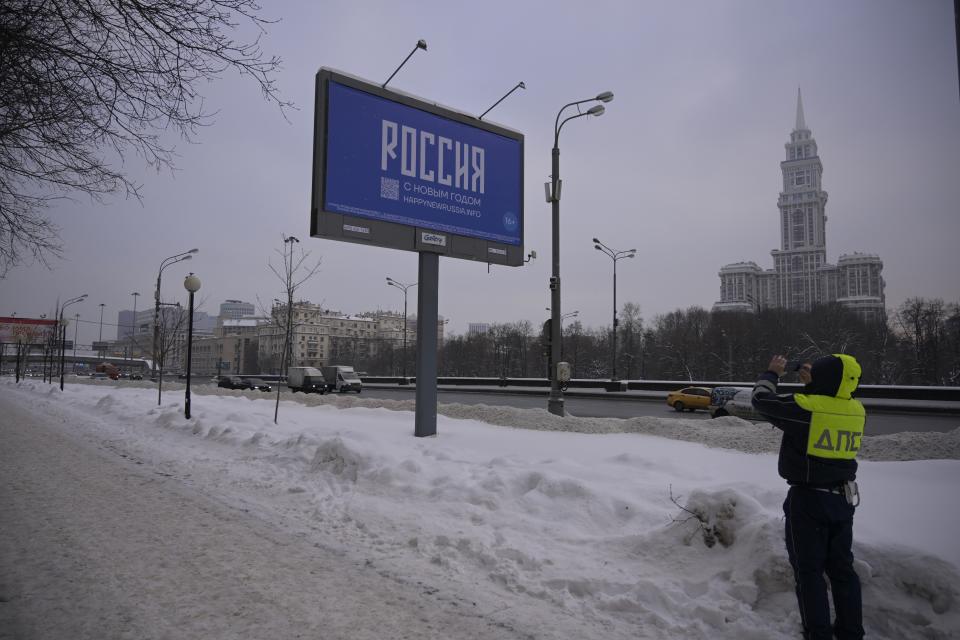 A traffic police officer takes a photo of a billboard with the words Happy New Year and the QR code in Moscow, Russia Thursday Dec. 7, 2023. Russia’s opposition have come up with a creative way of getting round censorship to call Russians to vote against President Vladimir Putin in the country’s upcoming March presidential elections — by taking out billboards under the guise of a new year greeting which leads to an anti-Putin website. (AP Photo)