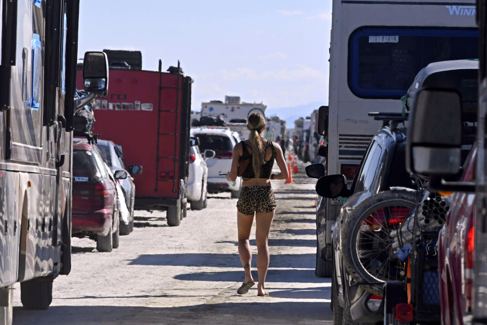 FILE - A woman walks between cars exiting the Burning Man festival, Sept. 5, 2023, in Black Rock Desert, Nev. Burning Man organizers don't foresee major changes in 2024 thanks to a hard-won passing grade for cleaning up this year's festival. Some feared their pledge to “leave no trace” might be too tall of a task after a rainstorm turned Nevada's high desert into a muddy quagmire, temporarily delaying the departure of some 80,000 revelers over the Labor Day holiday. (AP Photo/Andy Barron, File)