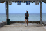 A woman wears a mask as she walks along a closed Waikiki Beach pier in Honolulu on Saturday, March 28, 2020. Like many cities across the world, Honolulu came to an eerie standstill this weekend as the coronavirus pandemic spread throughout the islands. But Hawaii officials went beyond the standard stay-at-home orders and effectively flipped the switch on the state's tourism-fueled economic engine in a bid to slow the spread of the virus. As of Thursday, anyone arriving in Hawaii must undergo a mandatory 14-day self-quarantine. The unprecedented move dramatically reduced the number of people on beaches, in city parks and on country roads where many people rely on tourism to pay for the high cost of living in Hawaii. (AP Photo/Caleb Jones)