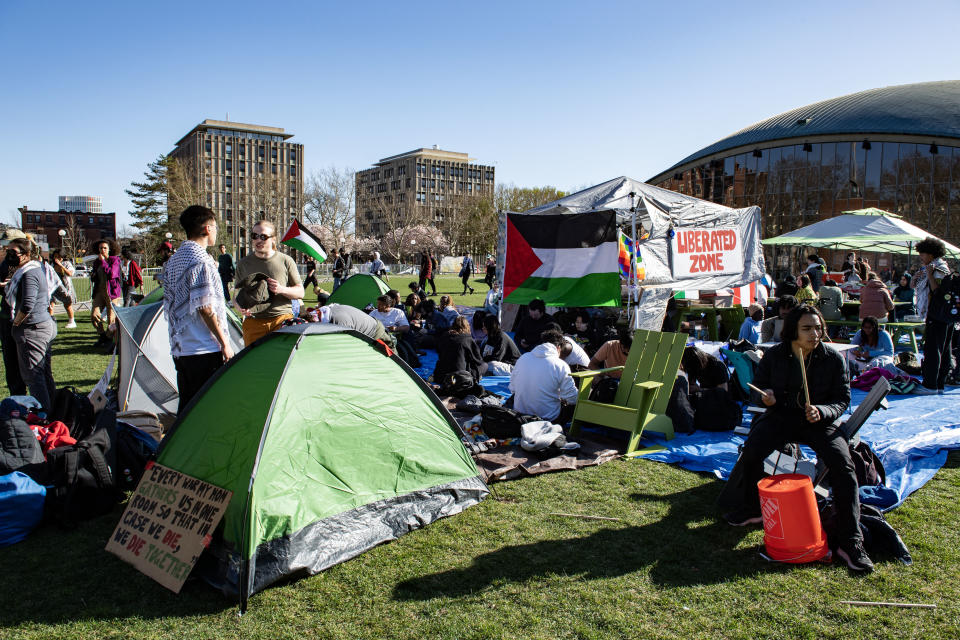 Group of people at an outdoor event with tents and a sign reading "LIBERATED ZONE."